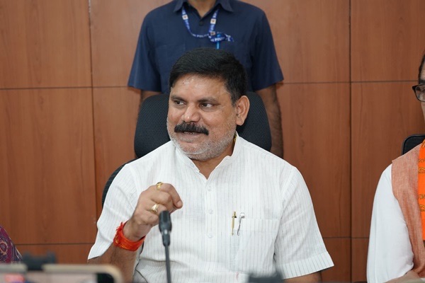 Satish Chandra Dubey seated at a meeting table, speaking and gesturing, with a microphone in front of him