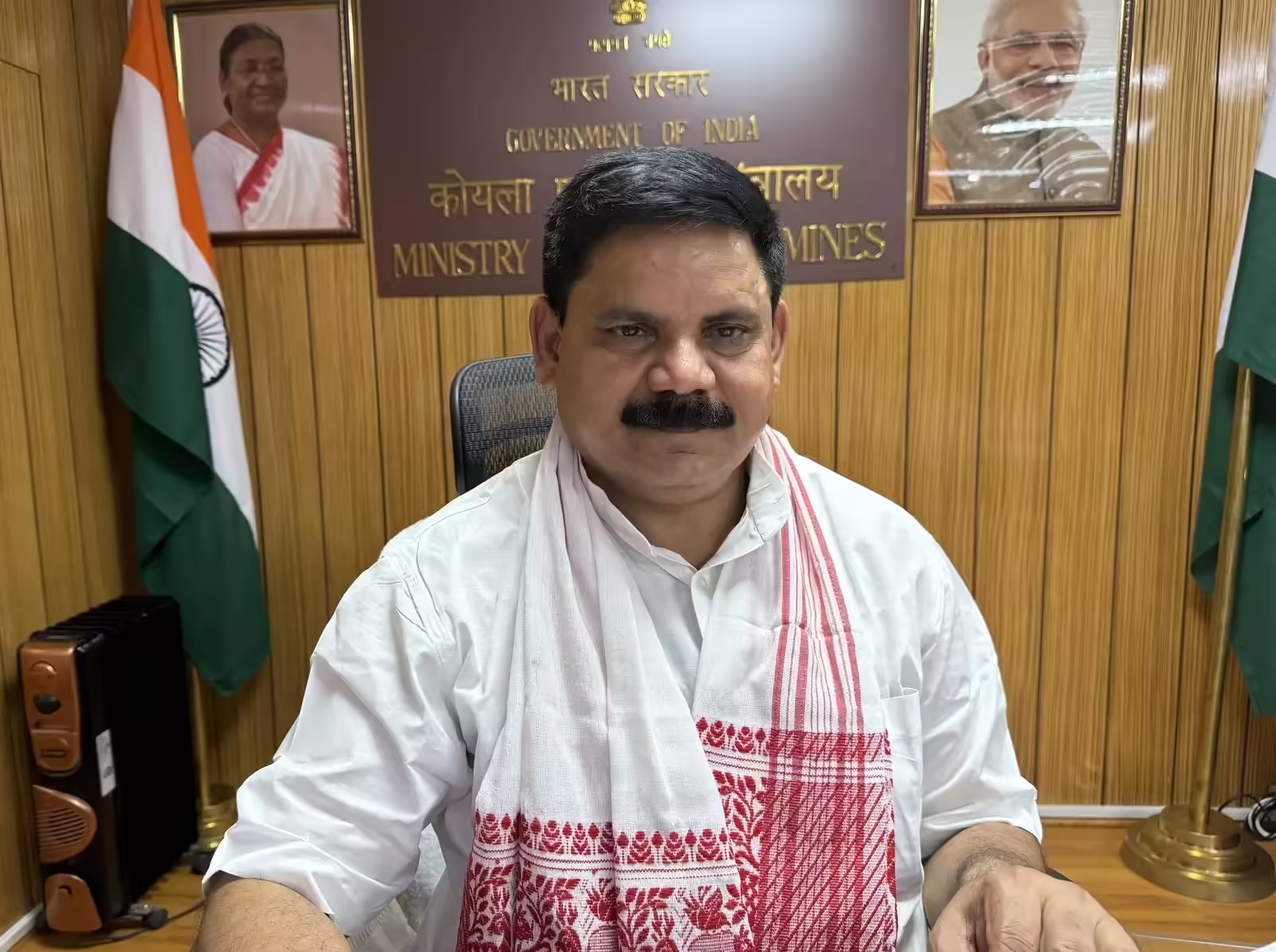 Satish Chandra Dubey seated at his desk in a white kurta and a red-and-white patterned stole, with the Government of India nameplate of the Ministry of Coal and Mines, the national flag and official portraits behind him