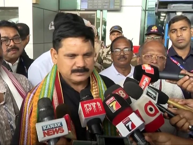 Satish Chandra Dubey, wearing a colourful woven stole, speaks to reporters holding microphones from several television channels