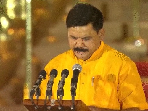Satish Chandra Dubey, in a yellow kurta, reads the oath of office at a lectern with microphones