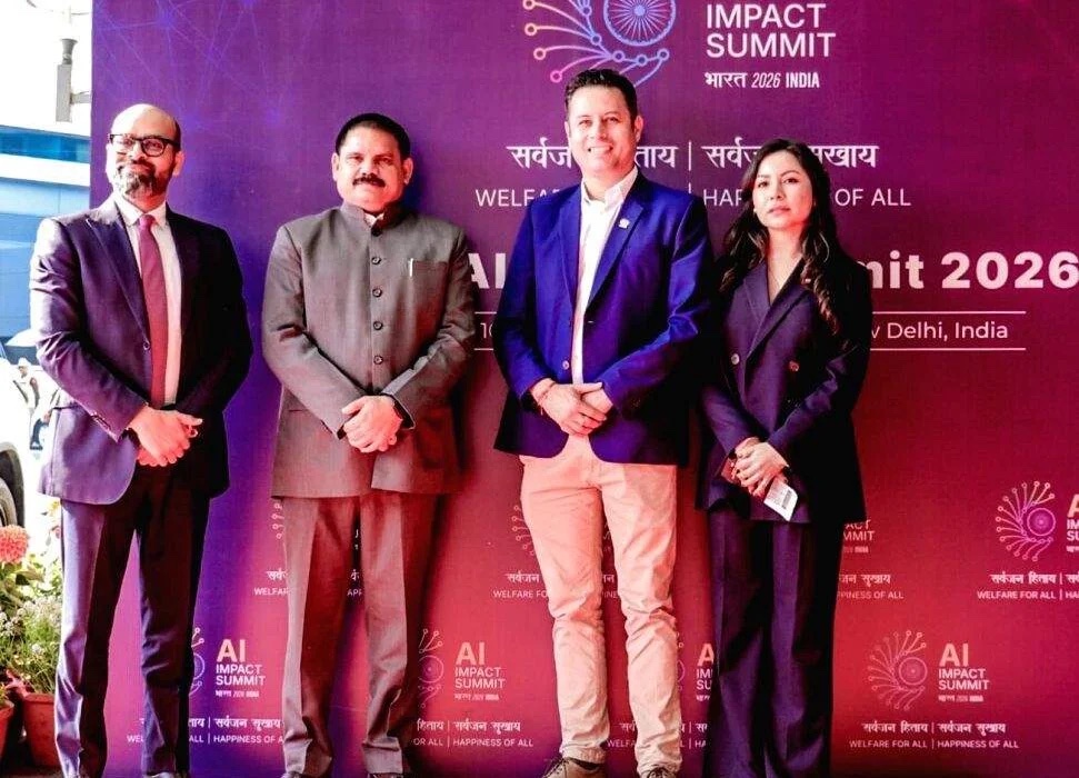 Satish Chandra Dubey in a grey bandhgala standing with three other attendees in front of the AI Impact Summit 2026 backdrop in New Delhi