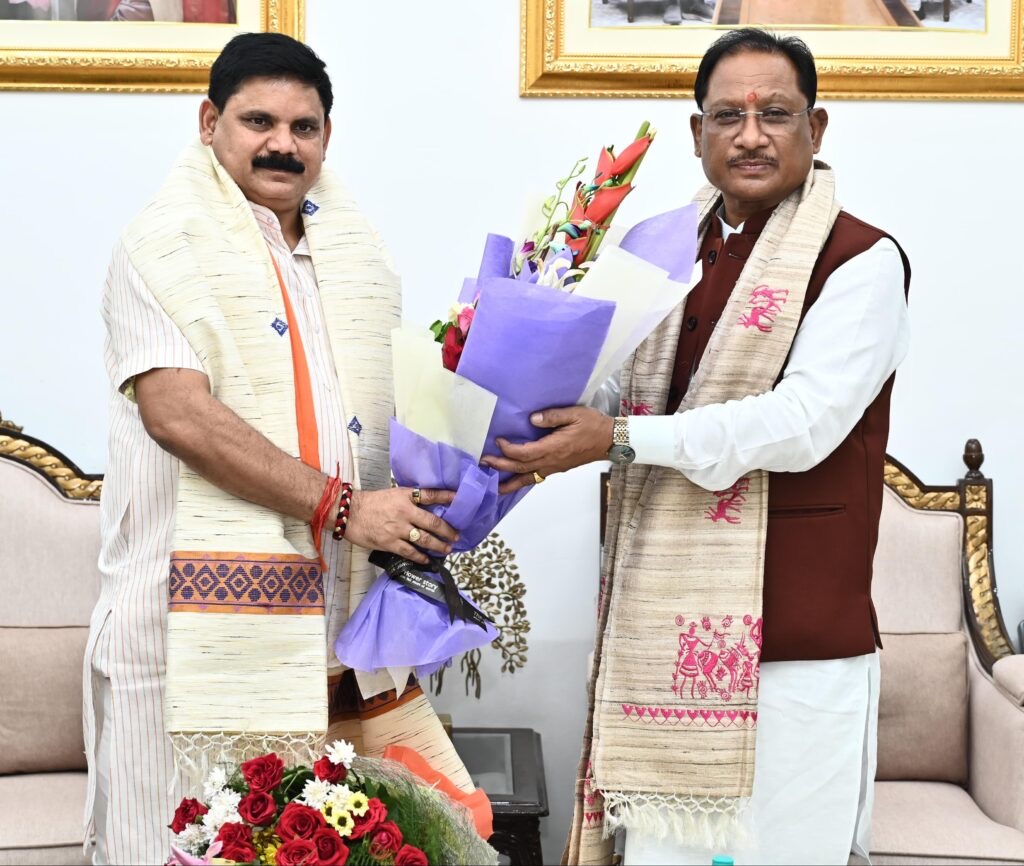 Satish Chandra Dubey, wearing a cream stole, receives a bouquet from Chhattisgarh Chief Minister Vishnu Deo Sai in a formal sitting room
